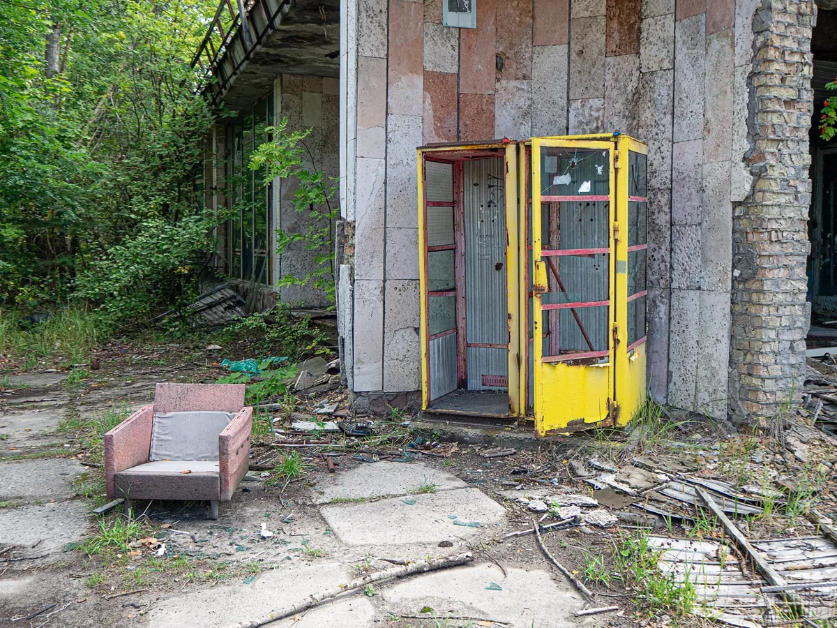 Verlassener Hof mit gelber Telefonzelle und einem rosa Sessel, überwuchert
