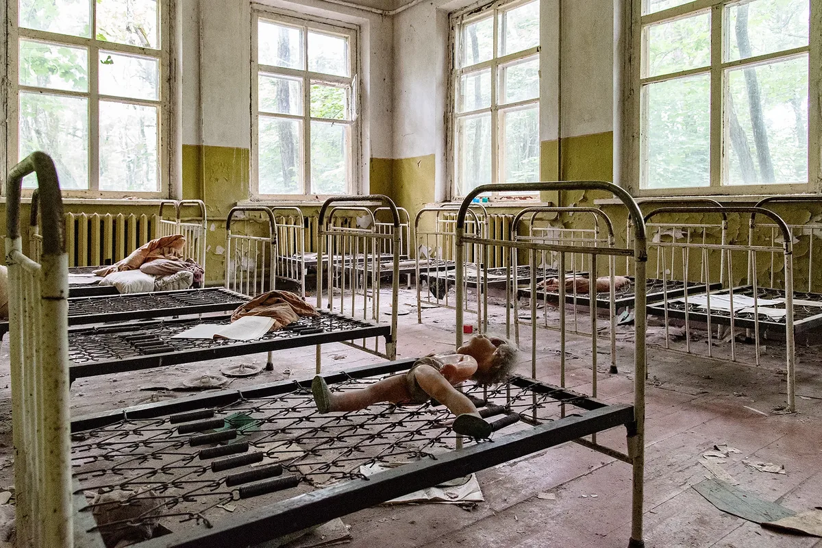 Verlassener Schlafsaal mit rostigen Bettgestellen und einer zurückgelassenen Puppe