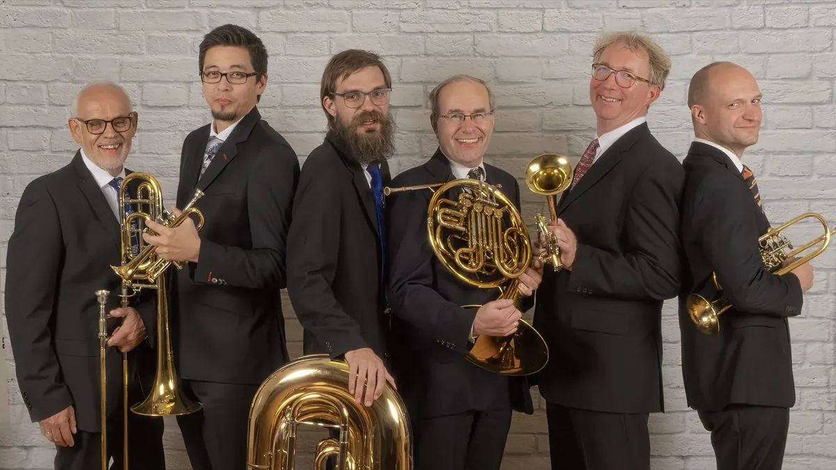 Blechbläserensemble mit sechs Musikern vor einer Ziegelwand