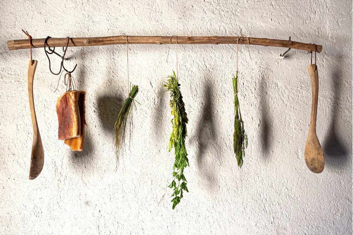 Küchenkräuter und Holzlöffel hängen an einer Stange vor weißer Wand